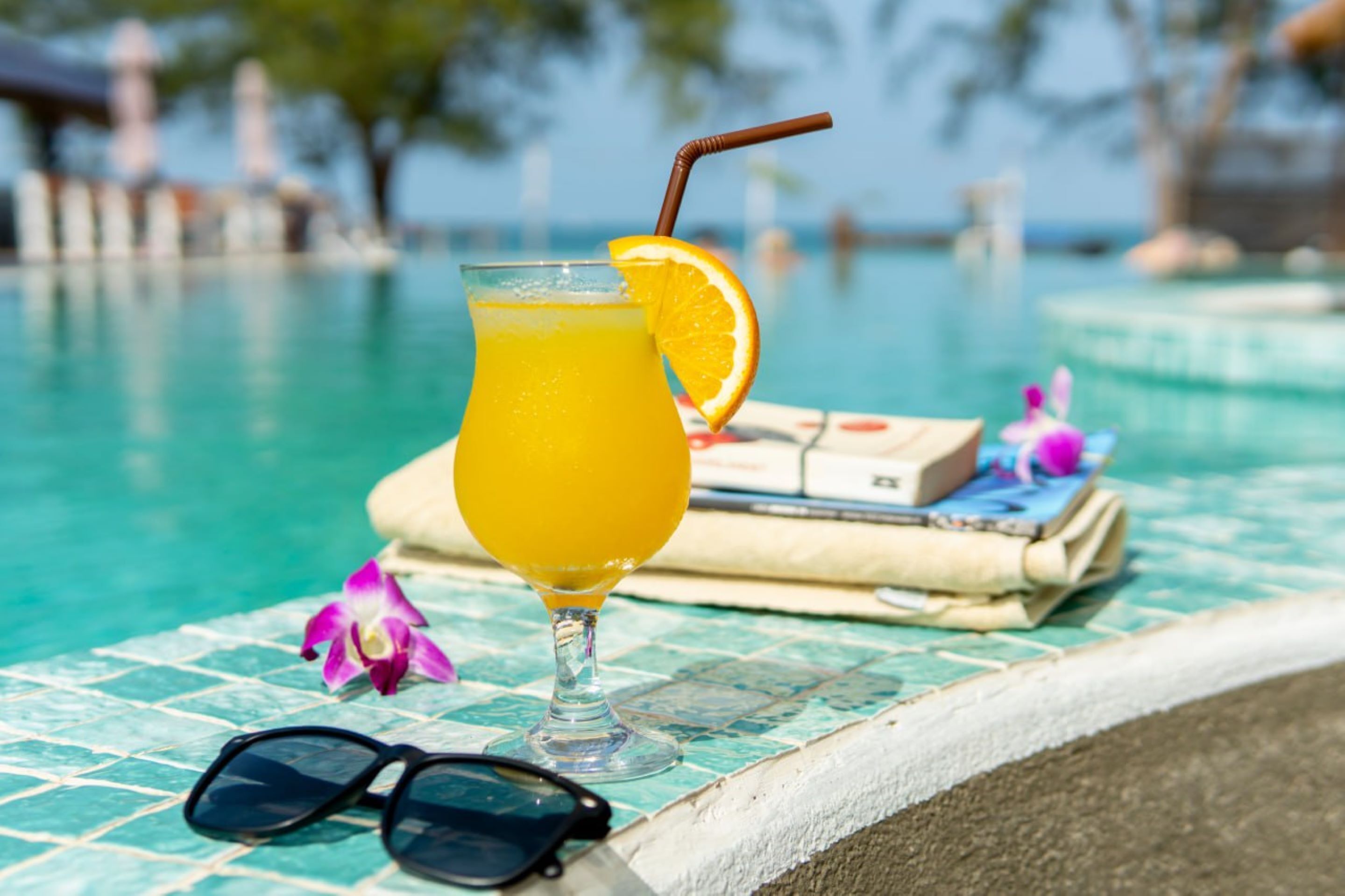 A glass of orange juice with a straw and an orange slice on a poolside table.