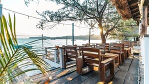 A wooden deck with benches overlooking a body of water, surrounded by trees and a thatched roof structure. - Sara Resort (Koh Rong Sanloem)