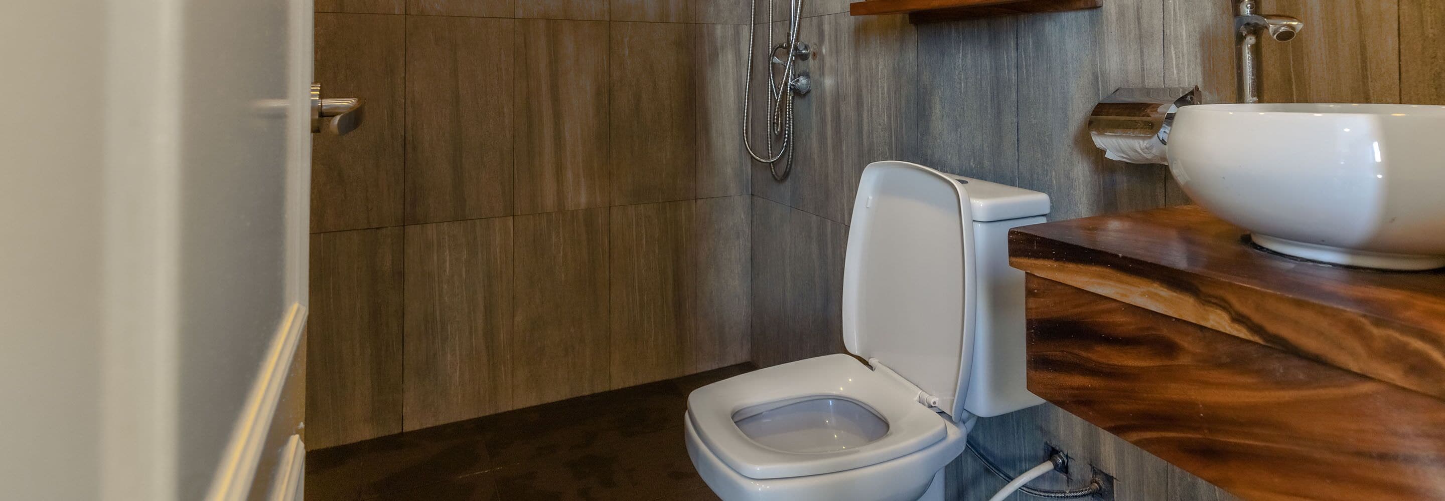 Un bany modern amb un moble de tocador de fusta, un vàter blanc i una zona de dutxa.