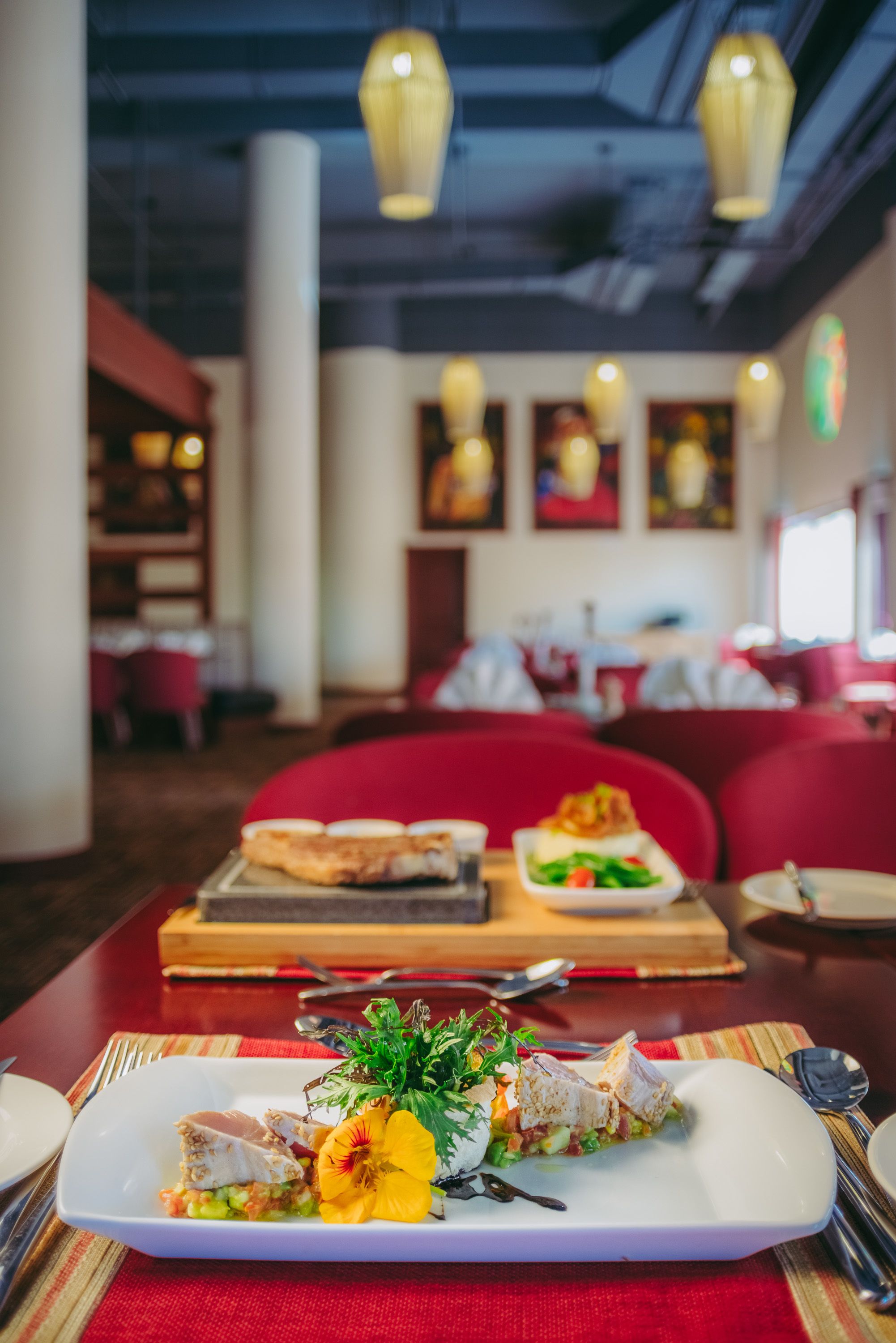 Een restaurant met een rode zithoek met banken en een eettafel met een bord eten en een houten plank.