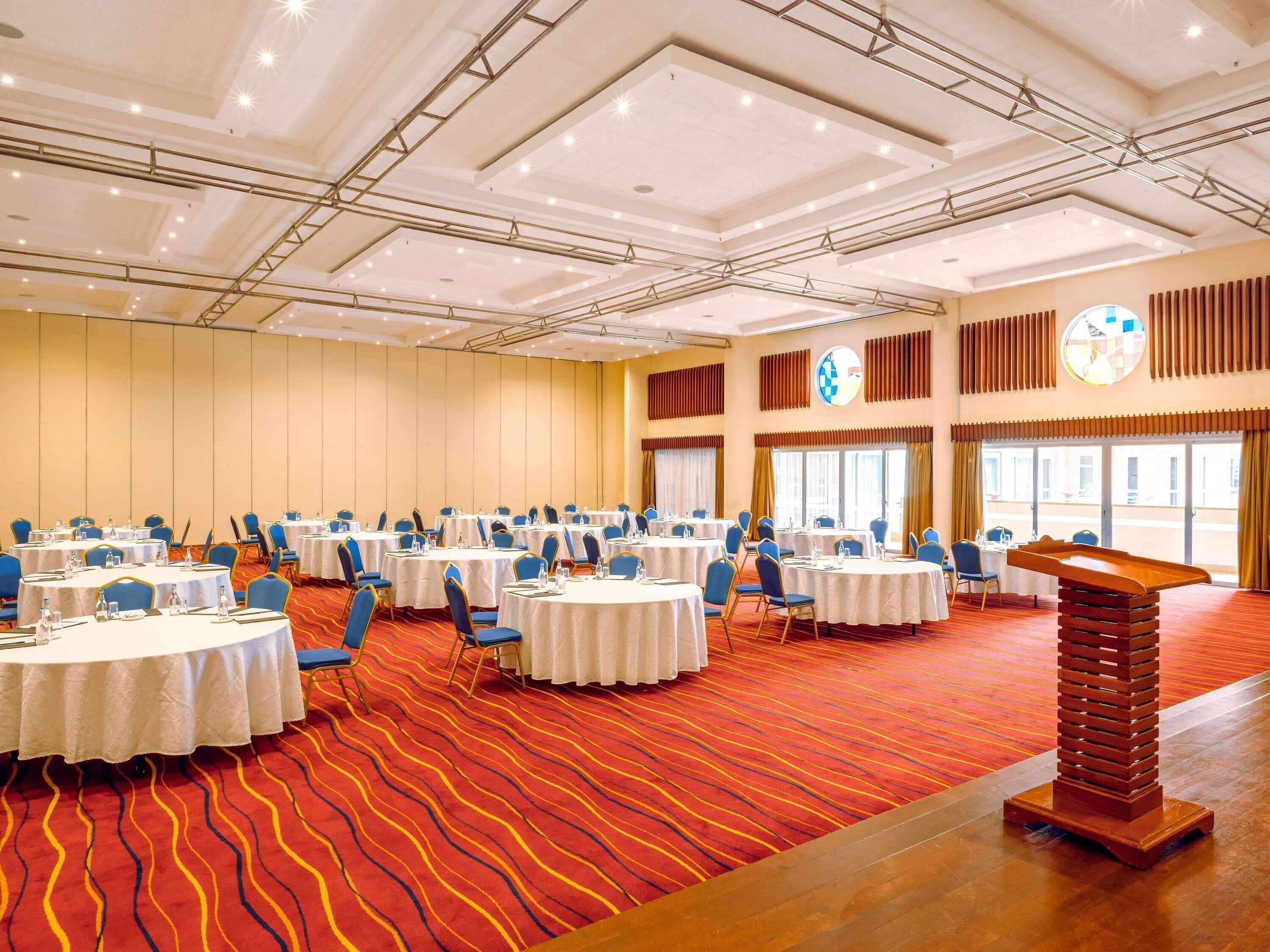 A large conference room with multiple round tables, blue chairs, and a pool table.