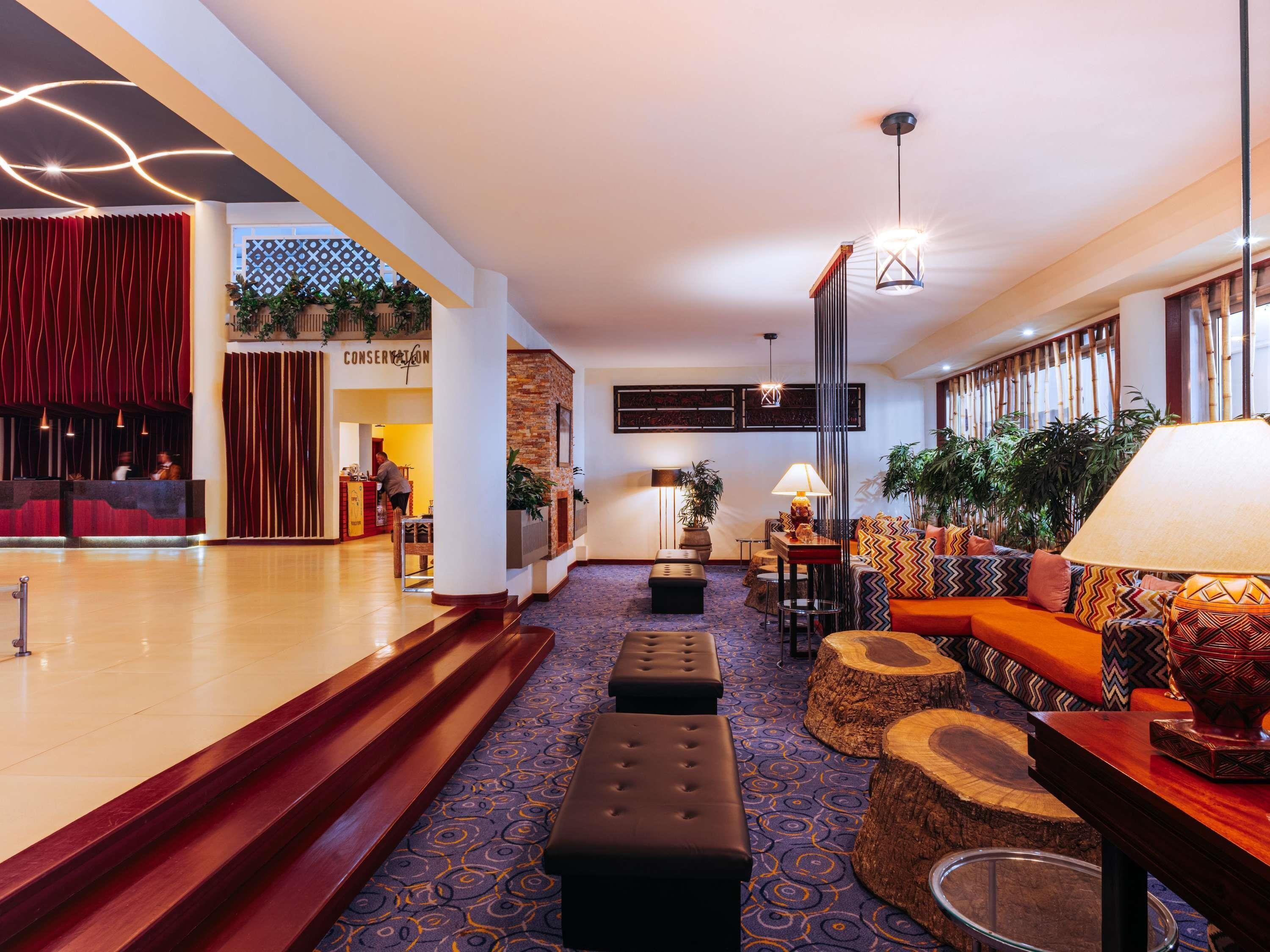 A hotel lobby with a reception desk, seating area, and a staircase leading to another level.