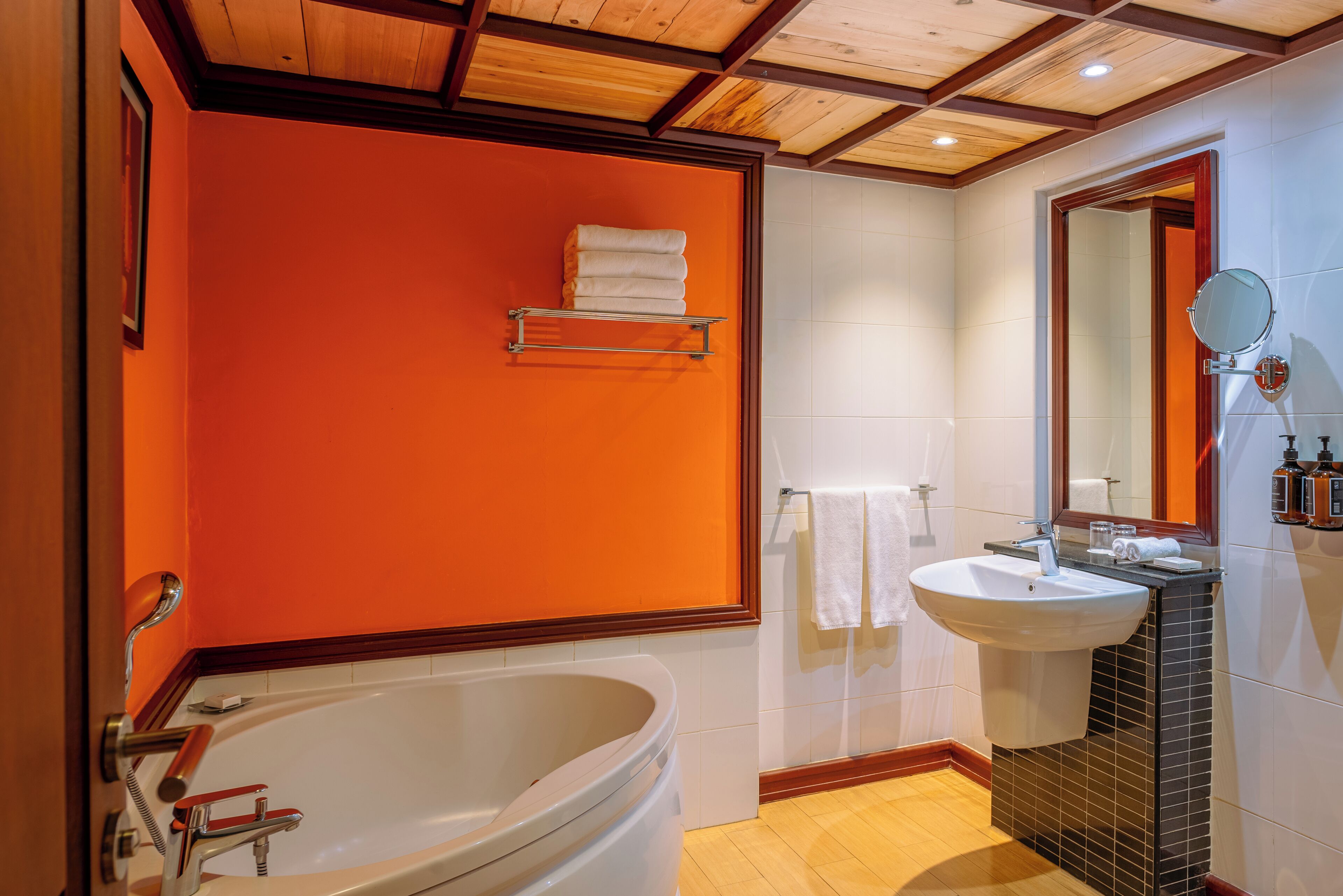 A bathroom with an orange wall, a white bathtub, a sink with a mirror, and a towel rack.