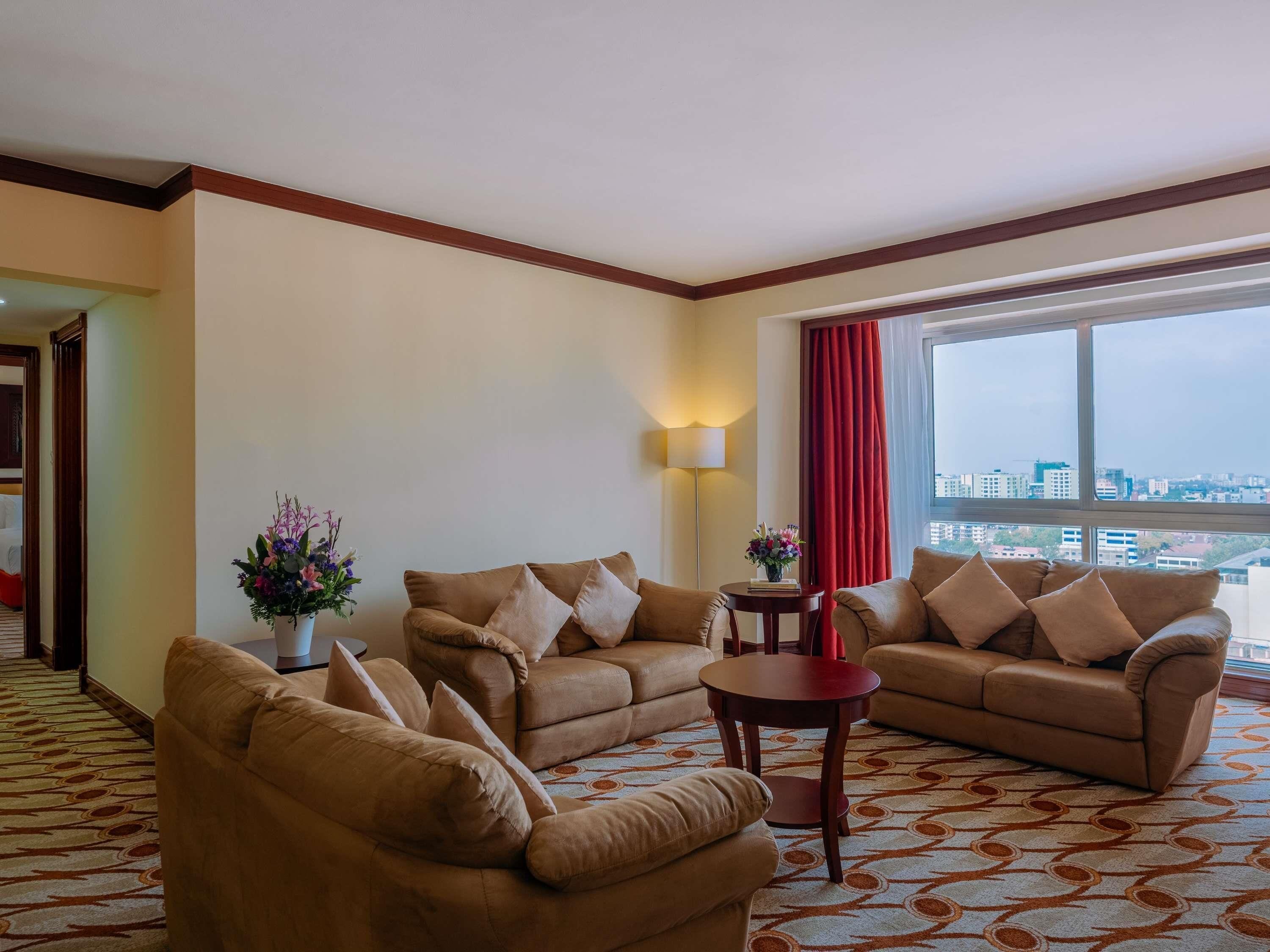 A hotel room with a large window, two sofas, a small table, and a lamp.