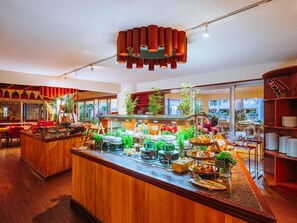 A modern restaurant with a wooden bar, various food displays, and a large window offering a view of the city.