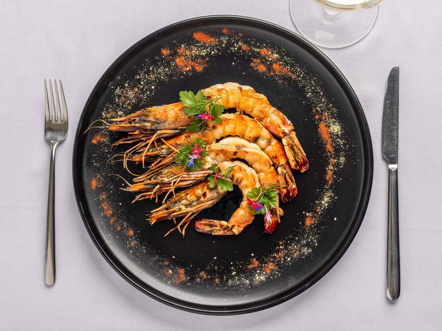 A black plate with grilled shrimp, garnished with parsley and red pepper flakes, on a white tablecloth.