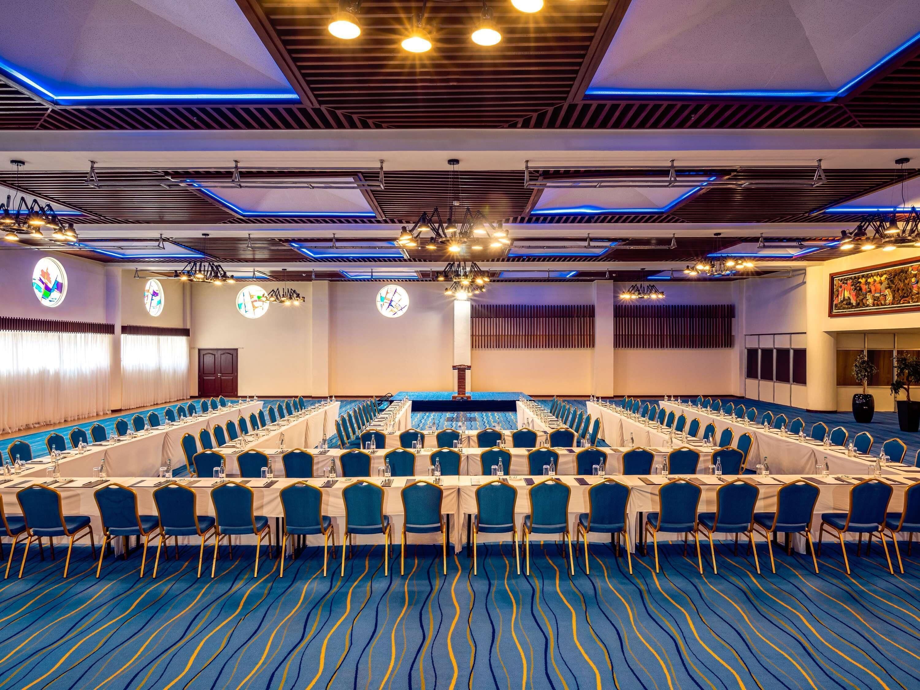 A conference room with a long table, blue chairs, and a patterned carpet.
