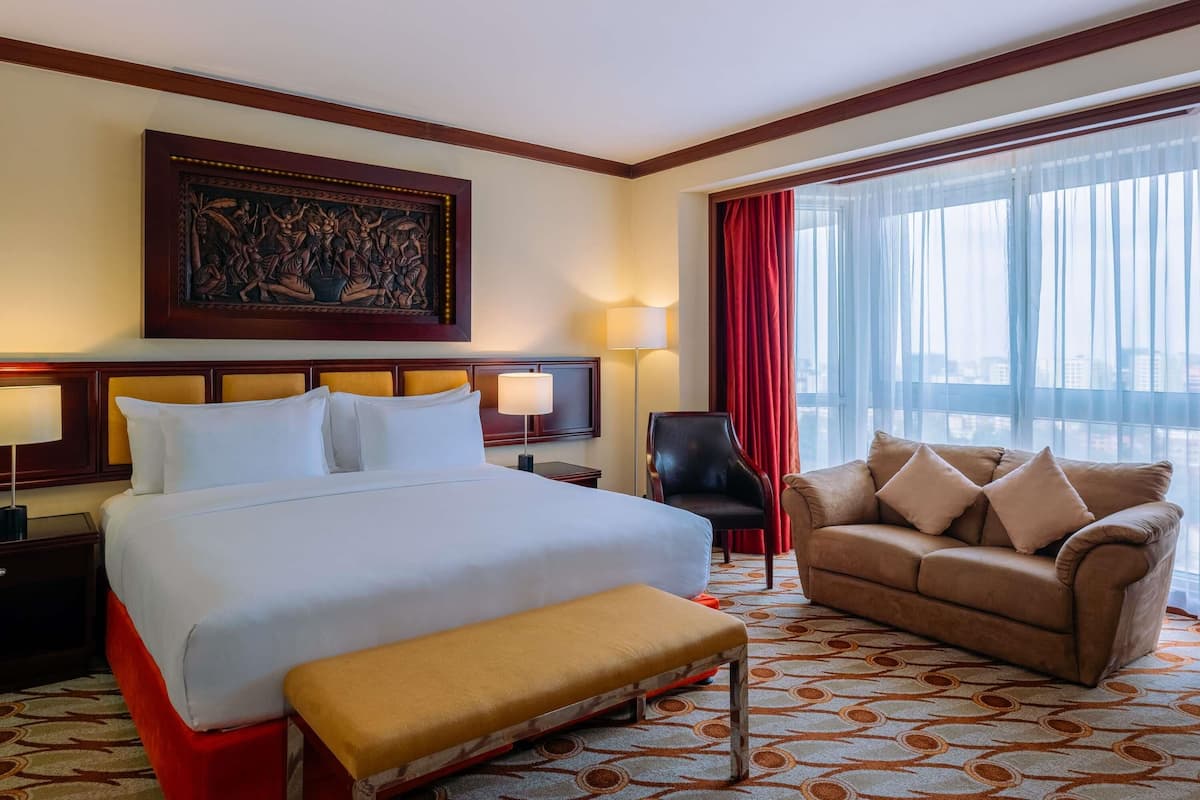 Een hotelkamer met een groot bed, een bank, een stoel, een bureau en een raam met gordijnen.