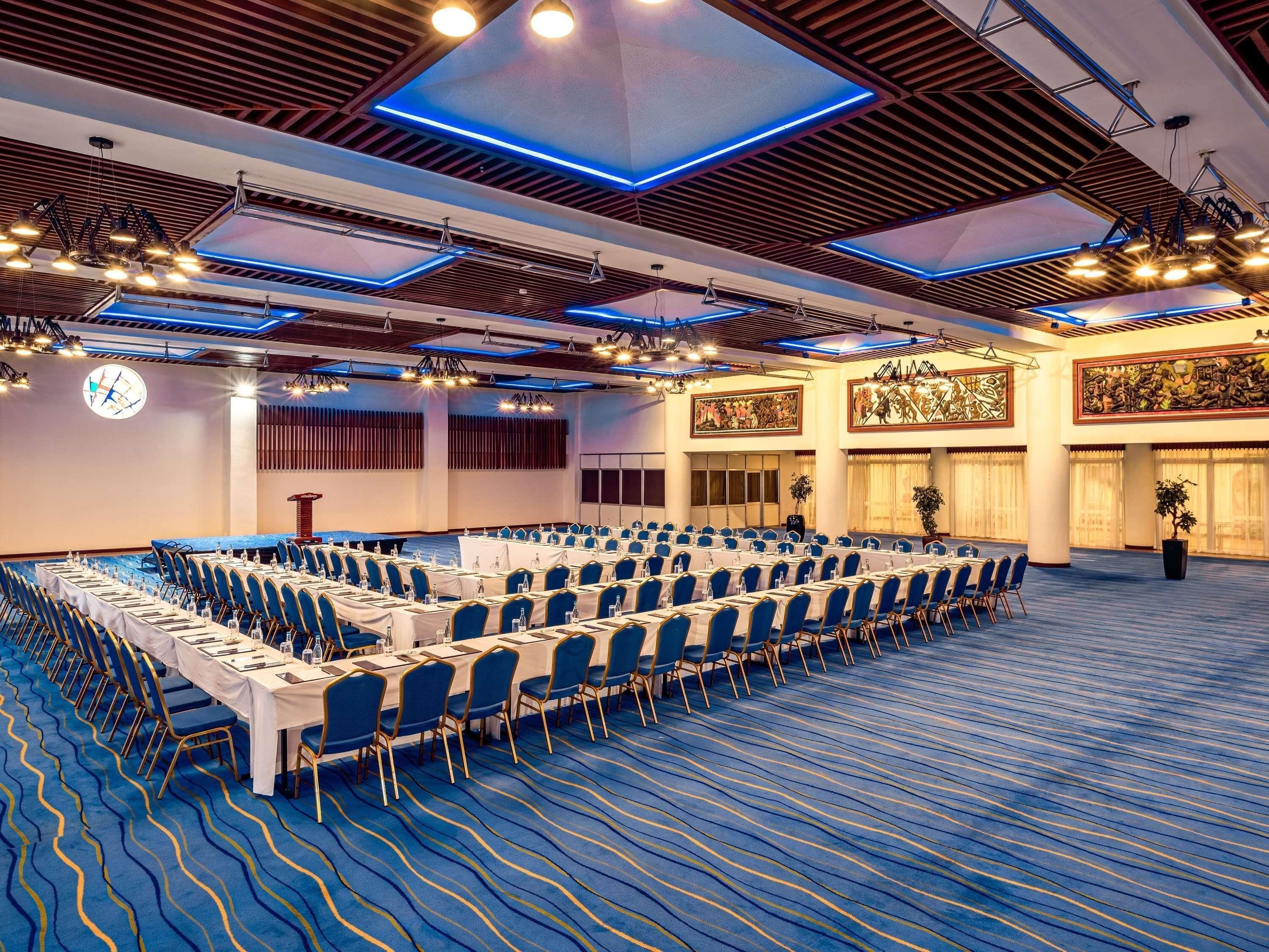 Une salle de conférence avec des rangées de tables et de chaises, une horloge et un grand lustre.