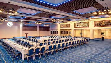 Une salle de conférence avec des rangées de tables et de chaises, une horloge et un grand lustre.