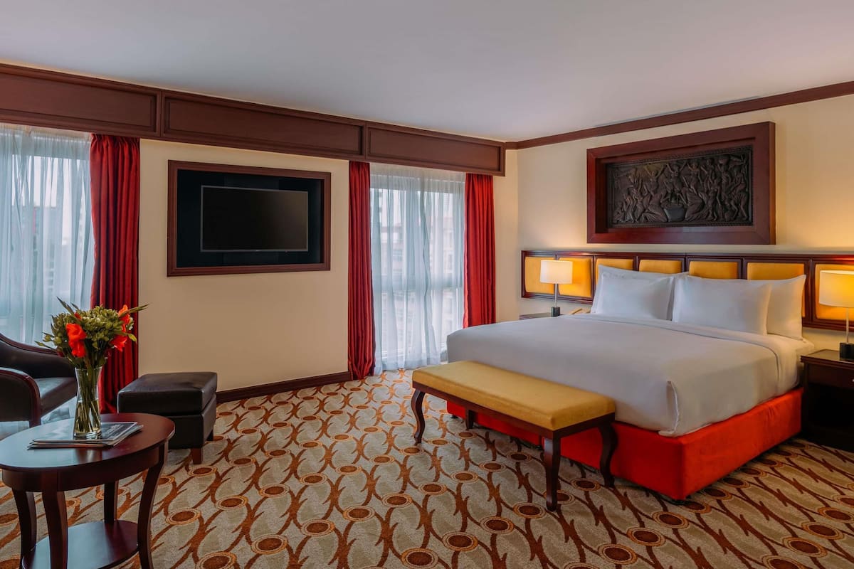 Een hotelkamer met een groot bed, een flatscreen televisie, een bureau met stoel, een bankje en een vaas met bloemen.
