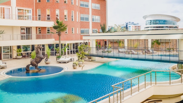 Une piscine ornée d’une statue de cheval, des chaises longues et un bâtiment à plusieurs étages doté de balcons.