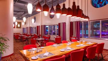 Une salle de conférence avec une longue table en bois, des chaises rouges et des luminaires suspendus.