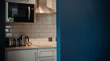 A kitchen with a microwave, toaster, kettle, and a stainless steel range hood.