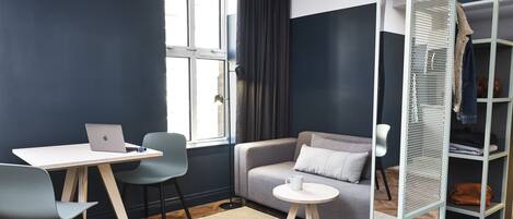 Una habitación moderna con escritorio, dos sillas, un sofá, una mesita y un zapatero.