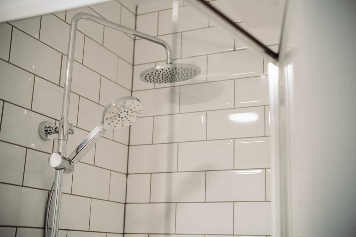 Eine Dusche mit Handbrause und Deckenbrause in einem gefliesten Badezimmer.