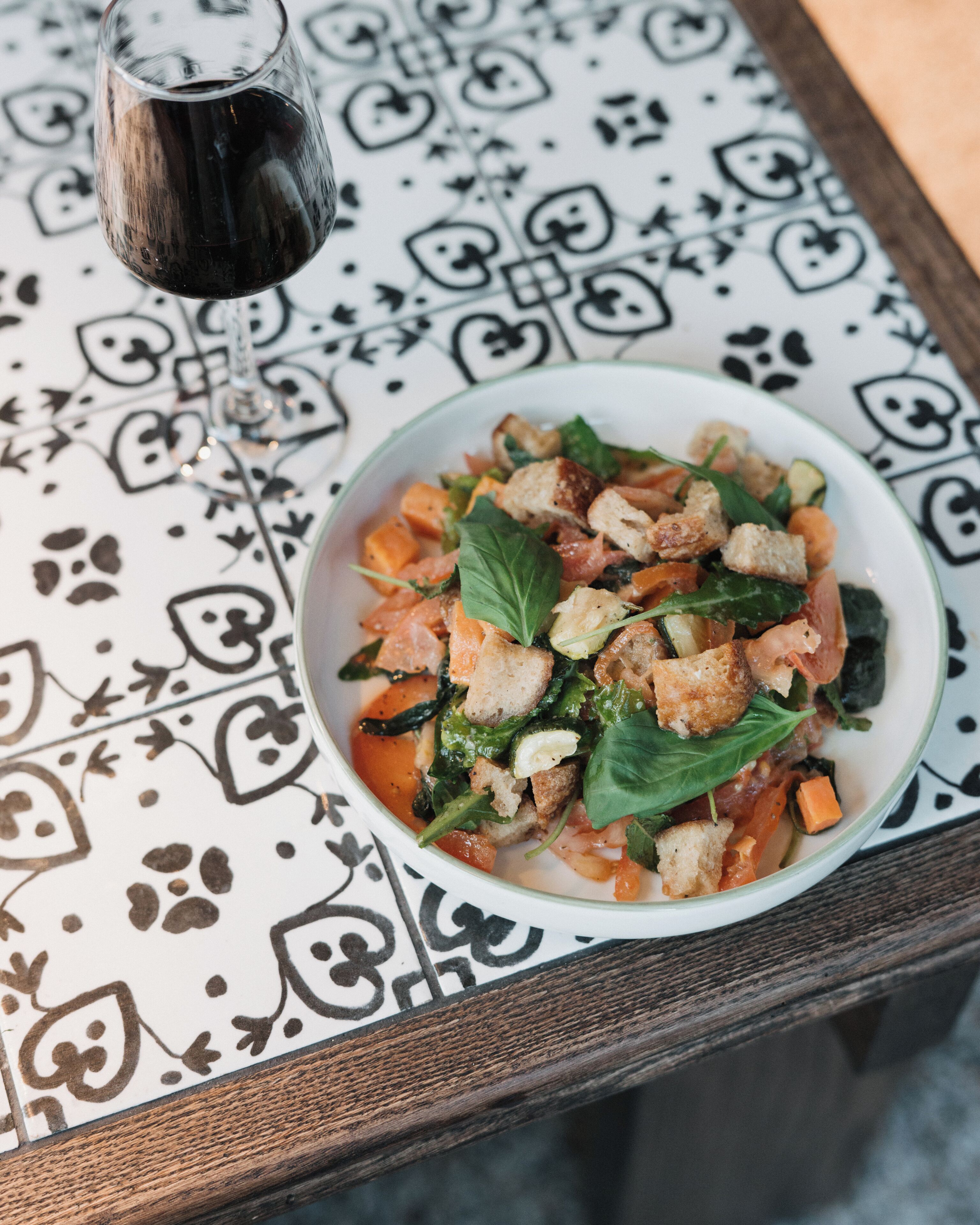 A bowl of salad with croutons and spinach on a patterned tablecloth.