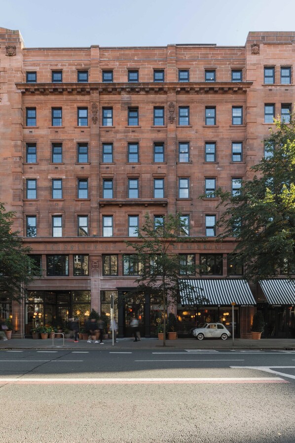A multi-story brick building with a central entrance, large windows, and a car parked in front.