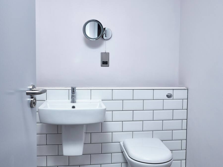 Casa de banho com lavatório branco, sanita e espelho fixado na parede.