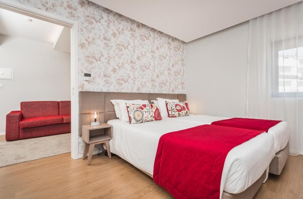 Un dormitorio moderno con una cama grande, un sofá rojo y una mesita de noche con una lámpara.