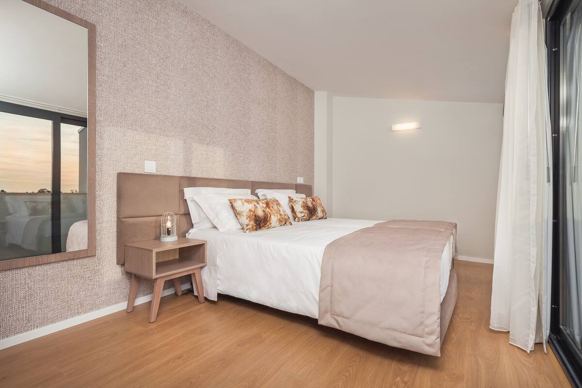 A modern bedroom with a large bed, a bedside table, a nightstand, and a mirror.