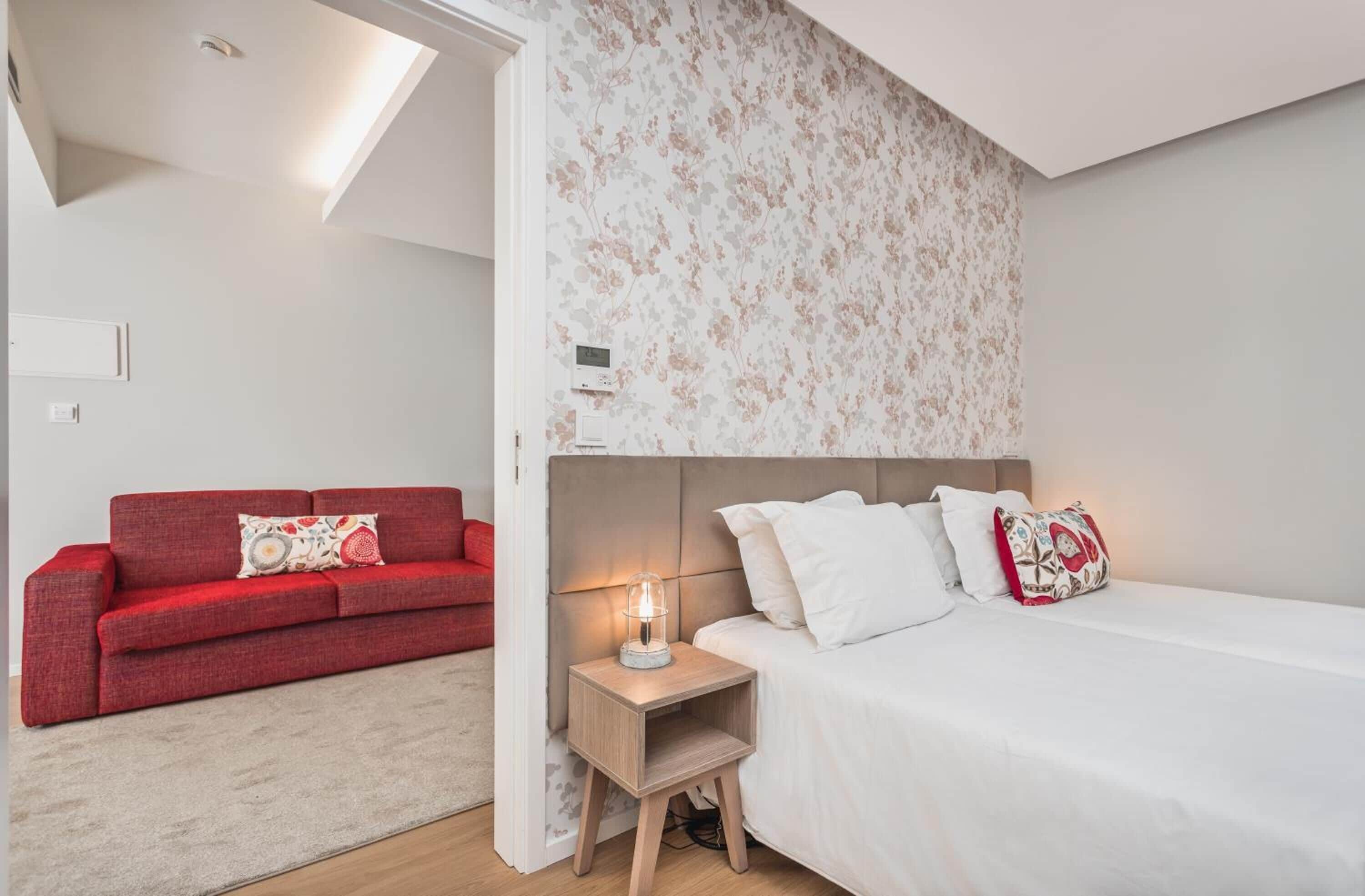 Un dormitorio con cama, mesita de noche y un sofá rojo en un apartamento moderno.
