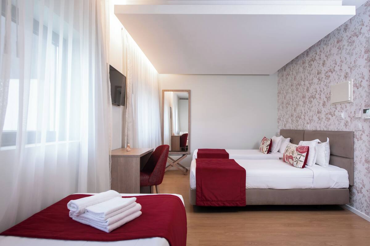 A hotel room with two beds, a desk, a chair, and a TV.