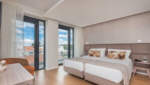 A hotel room with a large bed, a desk, and a view of the city through a glass door. - Essence Inn Marianos (Ourem)