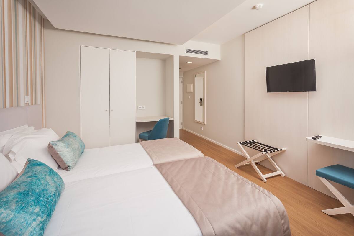 A modern hotel room with a bed, a desk, a chair, a TV, and a wardrobe.