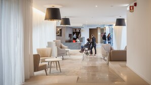 A hotel lobby with seating areas, a reception desk, and a glass partition. - Essence Inn Marianos (Ourem)