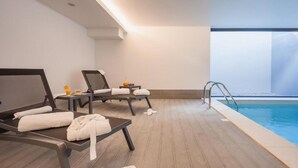 A spa area with two reclining chairs, a small table with a fruit bowl, and a pool with a glass railing. - Essence Inn Marianos (Ourem)