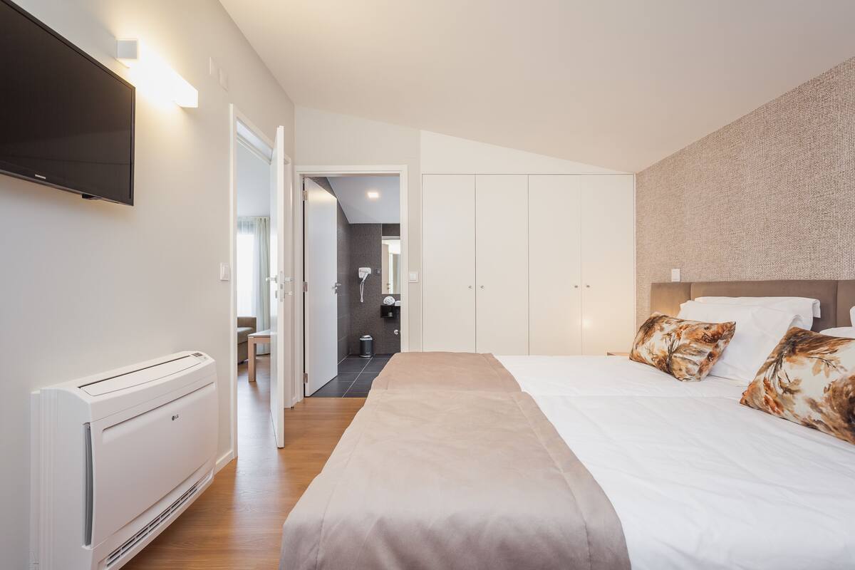 A modern hotel room with a large bed, a flat-screen TV mounted on the wall, and a walk-in closet.