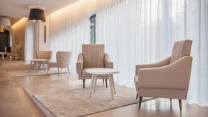 A modern hotel lobby with a seating area featuring a sofa and chairs, a round table, and large windows with sheer curtains. - Essence Inn Marianos (Ourem)