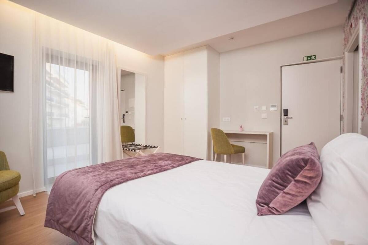 A hotel room with a bed, a desk, a chair, and a door with an exit sign.