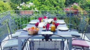 An outdoor dining area with metal chairs and tables, surrounded by lush greenery and potted plants. - Villa Tavallini (Pollone)