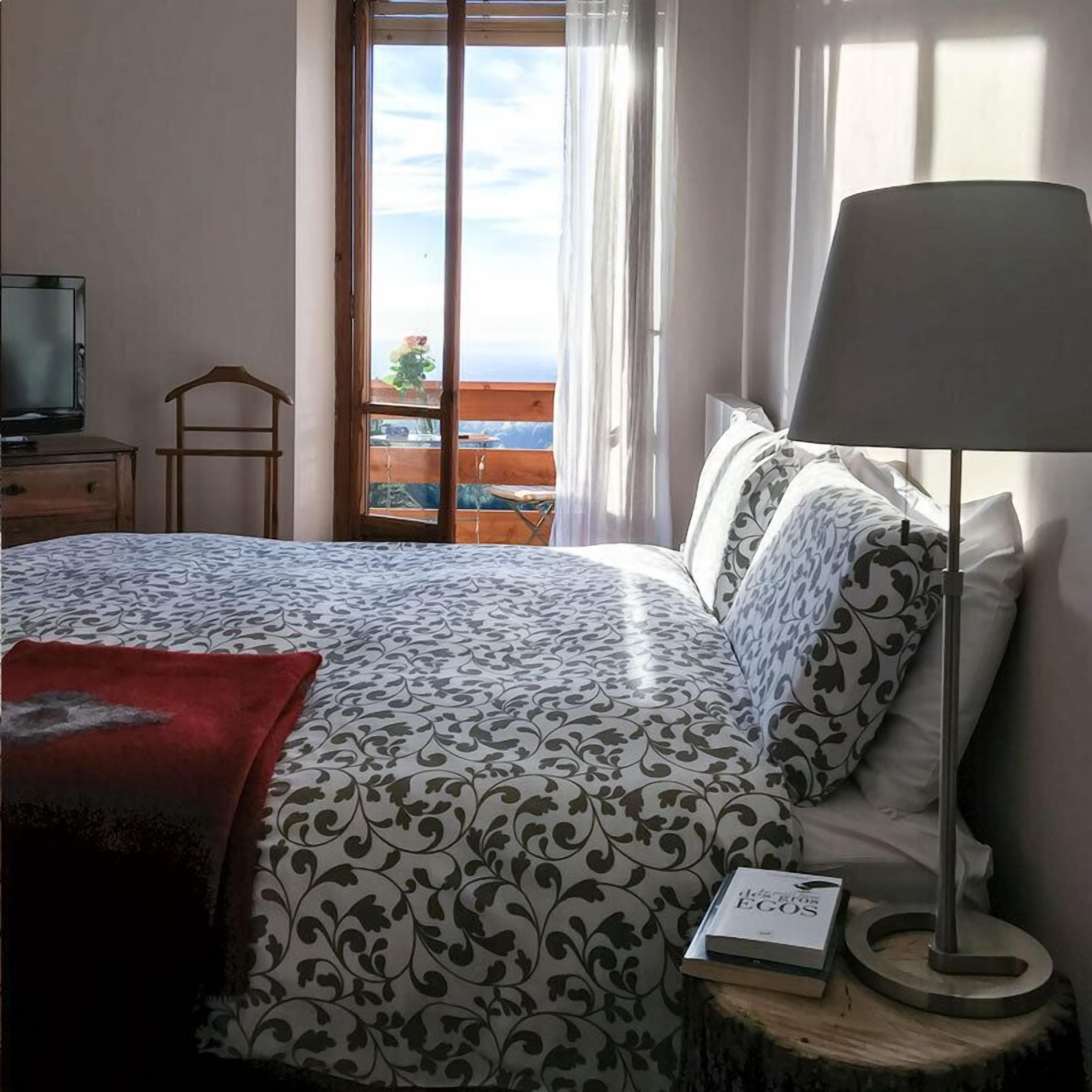 A bedroom with a bed, a bedside table with a lamp, a book, and a TV on a dresser.