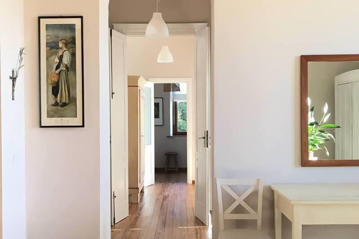 A room with a wooden floor, a white table, a framed painting on the wall, and a mirror on the right.
