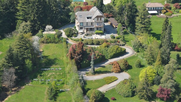 An aerial view of a large, two-story house with a winding driveway, surrounded by lush greenery and trees. - Villa Tavallini (Pollone)