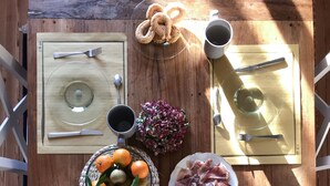 A round table set for a meal with plates, cutlery, a basket of bread, a bowl of fruit, and a cheese board. - Villa Tavallini (Pollone)