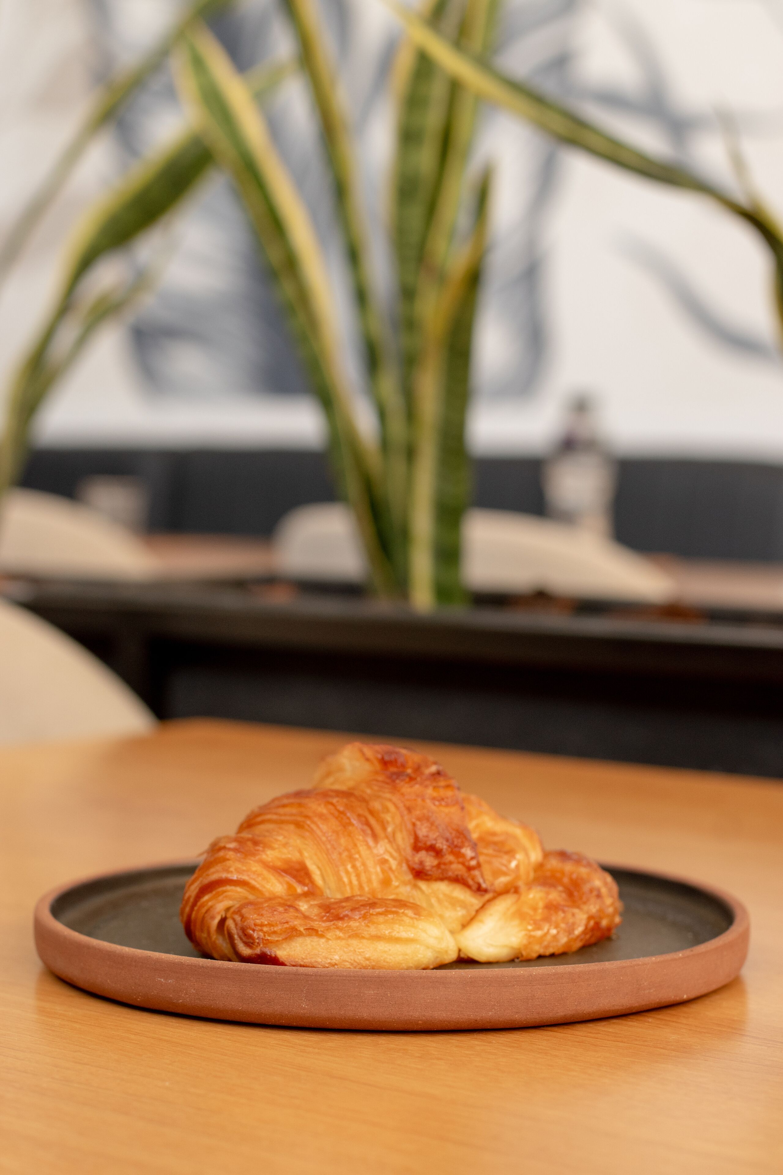 A croissant on a plate on a wooden table.