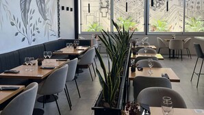 A restaurant with a modern interior, featuring a long dining table with chairs, a black cushioned bench, and a large potted plant in the center. - Days Inn & Suites by Wyndham La Plata (La Plata)
