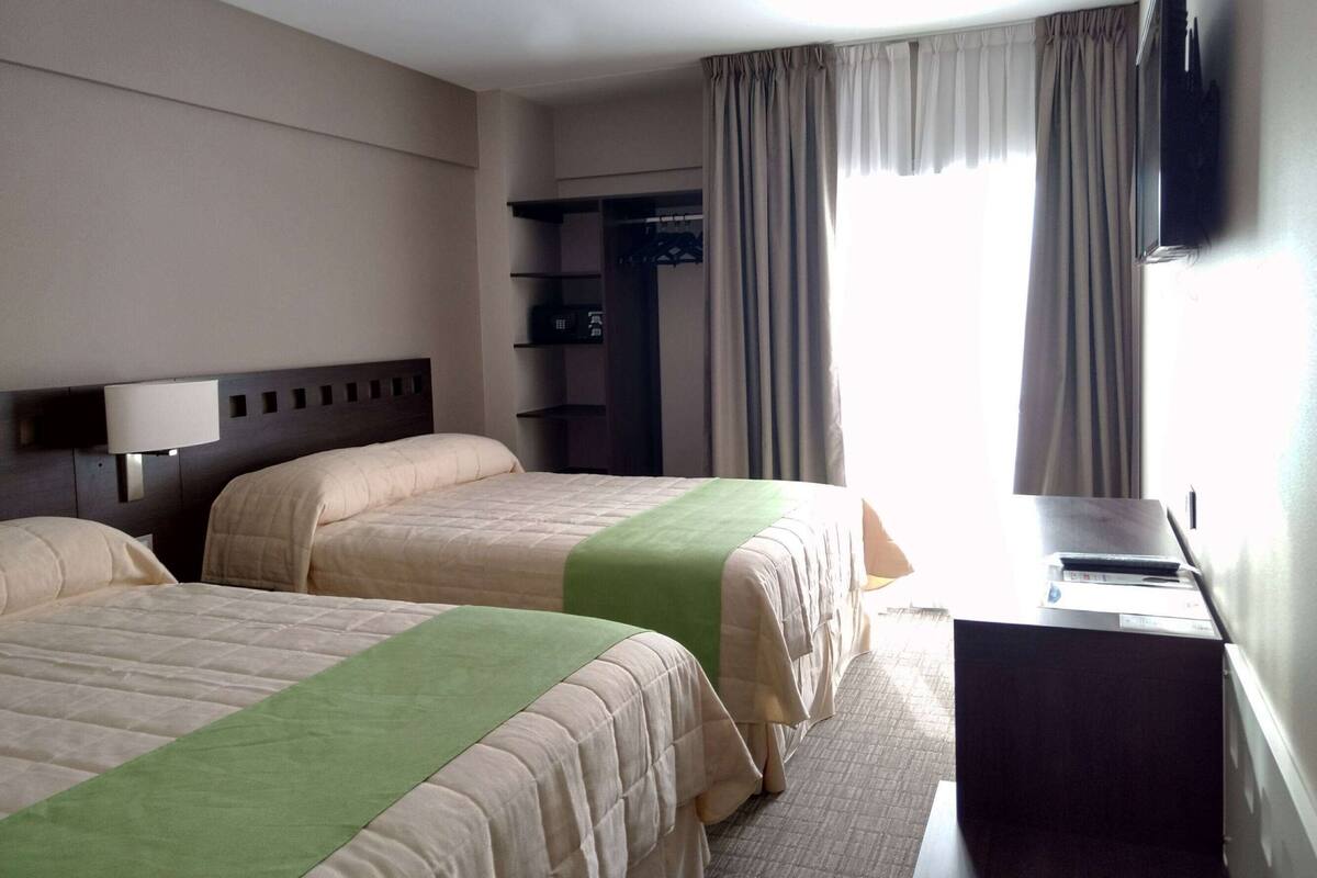 Ein Hotelzimmer mit zwei Betten, einem Schreibtisch, einem Fernseher und einem Kleiderschrank.