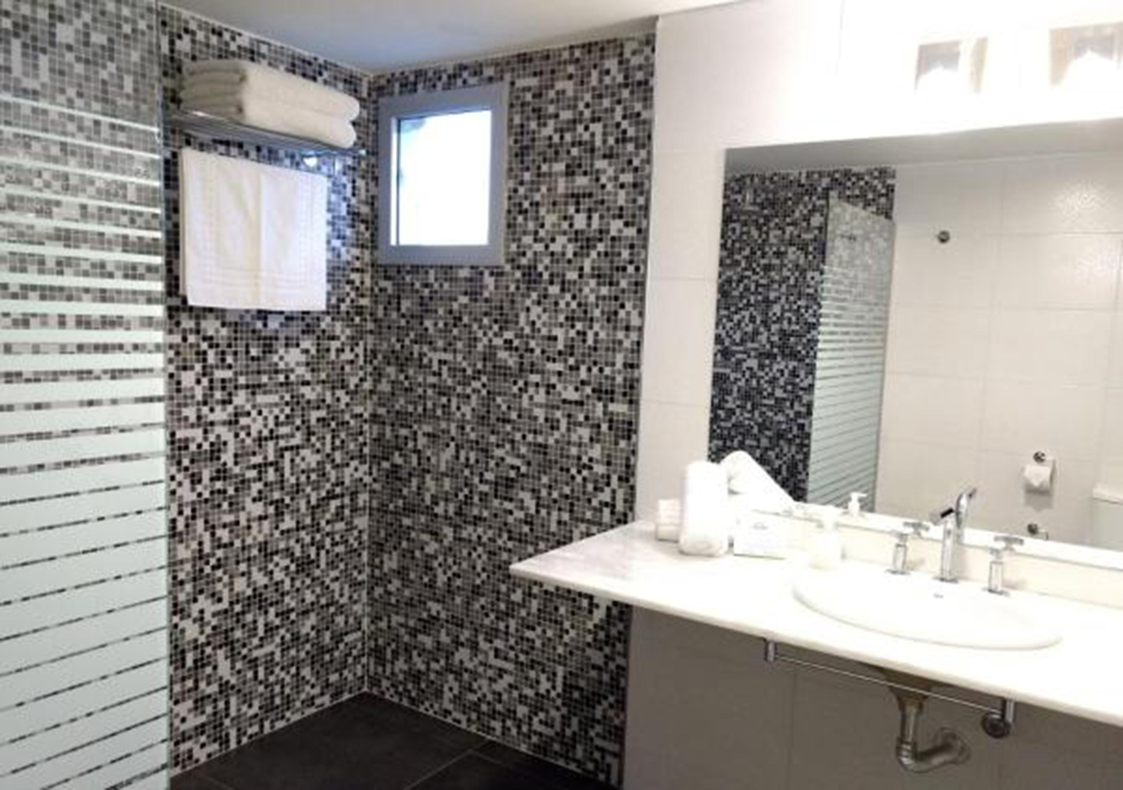 A bathroom with mosaic tile walls, a large mirror, and a white sink with toiletries.