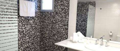 Een badkamer met mozaïektegel wanden, een grote spiegel en een witte wastafel met toiletartikelen.