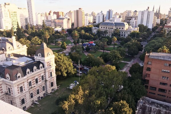 Un paisaje urbano con un edificio histórico grande, rodeado de árboles y modernos rascacielos.