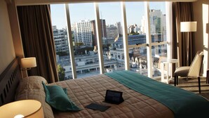 A hotel room with a large bed, a laptop, and a view of the cityscape through large windows. - Days Inn & Suites by Wyndham La Plata (La Plata)