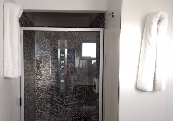 Un baño moderno con cabina de ducha de vidrio, paredes alicatadas y una toalla blanca colgada en la pared.