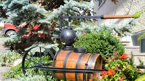 A decorative barrel with a spigot and a handle, surrounded by greenery and flowers. - Antica Residenza de Poda (Contà)