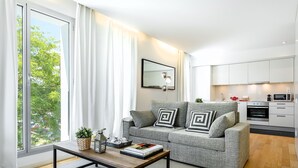 A modern living room with a grey sofa, a wooden coffee table, and a large window with white curtains. - Urban District - Rambla Suites & Pool (Barcelona)