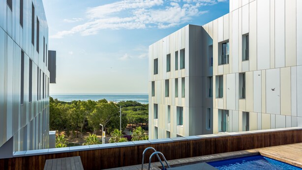 A modern building with a pool area, large windows, and a view of the ocean. - Urban District - Rambla Suites & Pool (Barcelona)